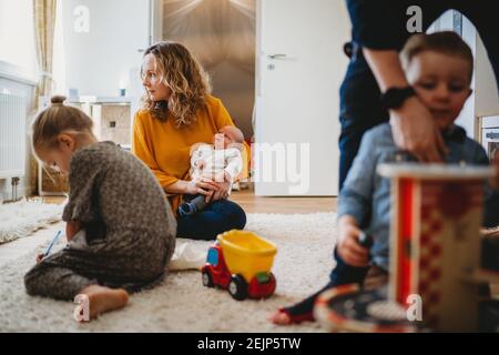 Family scene at home mom holding baby dad playing with children Stock Photo