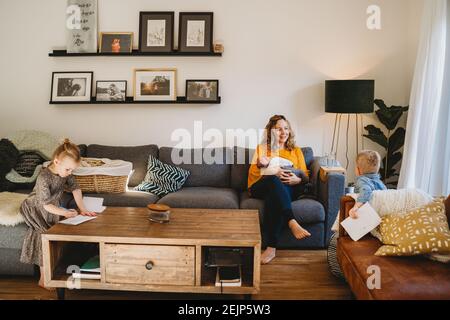 Happy mom in living room breastfeeding baby and talking to older kids Stock Photo