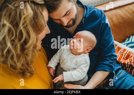 Newborn baby smiling at his parents sitting on sofa at home Stock Photo