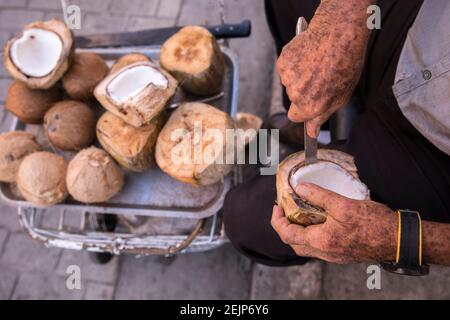 Old man's hands cutting coconut meat out of coconut with knife. Stock Photo