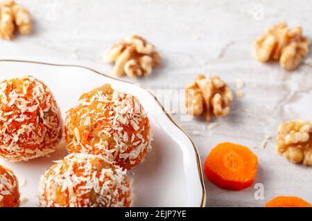 A kitchen countertop with a flat porcelain plate. Homemade fresh carrot bliss balls (mixture of cookie crumbles, walnut and carrot puree) coated with Stock Photo