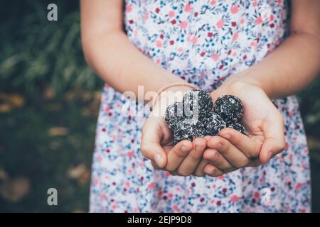Child in a flower dress holding chocolate healthy treats or bliss balls in a garden setting. Stock Photo