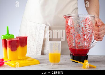 A mother is preparing homemade all natural fruit popsicles. She is filling bpa free plastic molds with layers of pureed mango and berry medley before Stock Photo