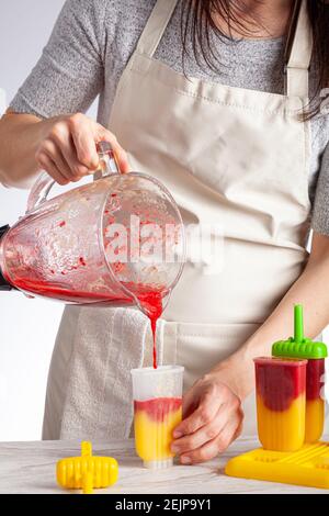A mom is preparing homemade all natural fruit popsicles. She is filling bpa free plastic molds with layers of pureed mango and berry medley before fre Stock Photo