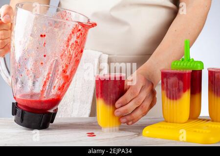 A mom is preparing homemade all natural fruit popsicles. She is filling bpa free plastic molds with layers of pureed mango and berry medley before fre Stock Photo