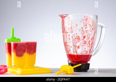 Close up isolated image of ice pop molds on a tray filled with homemade berry and mango puree with the glass bowl in the background. The mixture in th Stock Photo
