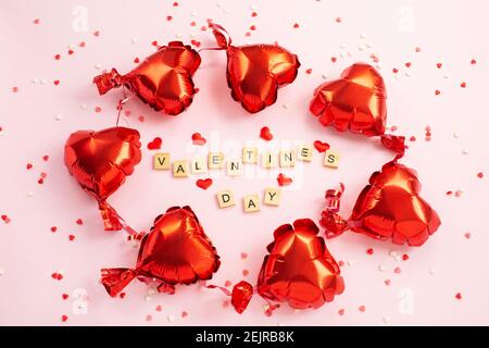 The word Valentine s Day from letter blocks and red hearts Foil balloons around. Romantic, St Valentines day concept. Top view. Stock Photo