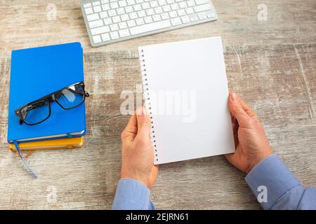 Hand of man holding an open notebook on wooden office desktop. Business report, Top view Stock Photo