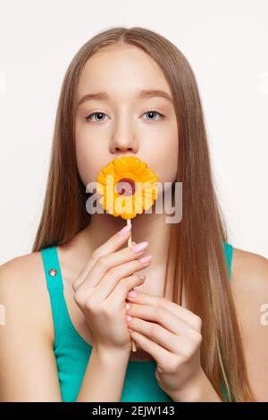 Teenager girl with flower lollipop in hands closing mouth. Sweet tooth concept. Stock Photo