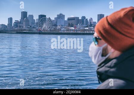 Young man wearing protective mask for Coronavirus protection looking at Montreal skyline Stock Photo