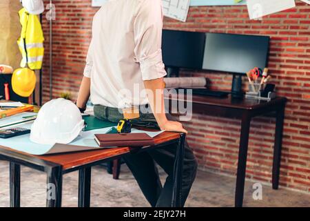 industry manager, engineer, businessman sitting on table and checking blueprint, drawing plan on the wall in the room in office. Stock Photo