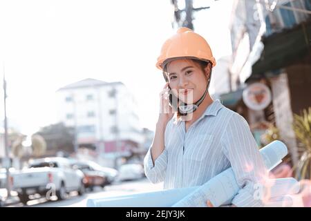 architect woman use mobile phone call with enginner or project manager between survey and checking at site construction. Architect woman hold blueprin Stock Photo