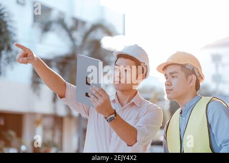 Architecture or engineerman and businessman survey and check at site construction with tablet and them wearing safety helmet in hot weather day. Archi Stock Photo