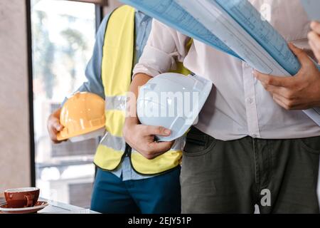engineer hold engineer drawing design blueprints and safety helmet in room at site construction. Stock Photo