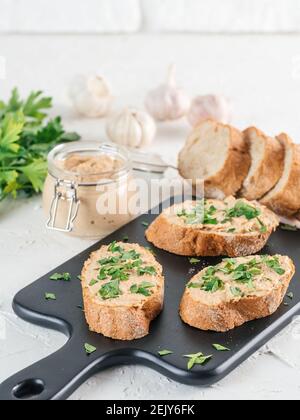 Close up view of slice bread with homemade turkey pate and fresh green parsley on black kutting board over white concrete background, Copy space. Stock Photo