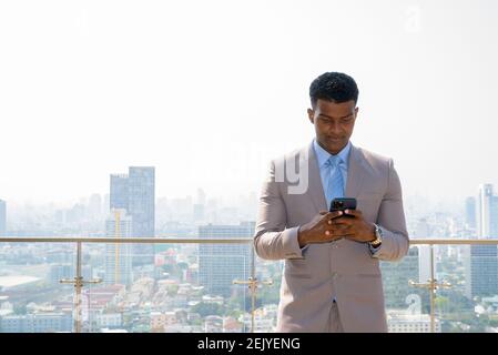 Portrait of handsome young African businessman wearing suit and using mobile phone Stock Photo