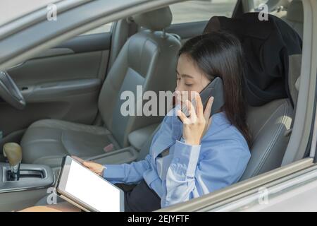 Businesswoman inside a car using a tablet and mobile phone for working. Stock Photo