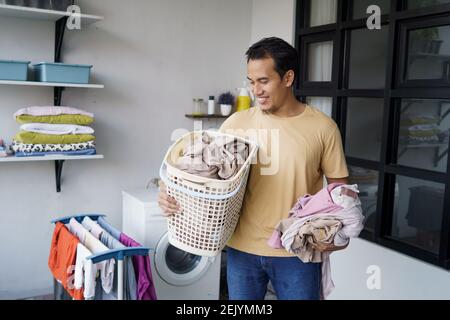 Housework. asian Man doing laundry at home loading clothes into washing machine Stock Photo