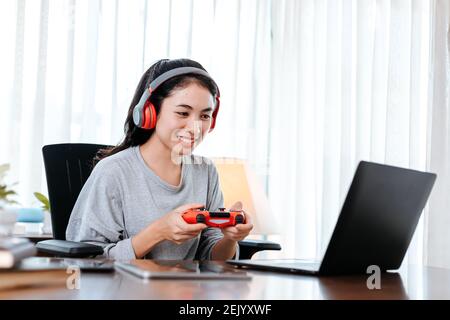 Funny Young woman wearing earphones playing computer game on laptop with joypad. Stock Photo