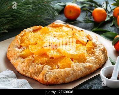 Close up view of caraway and orange tart on baking paper over black cement background. Winter season and christmas ideas recipe - tart with caraway pastry and oranges, mandarines or tangerines. Stock Photo