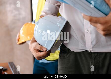 engineer hold engineer drawing design blueprints and safety helmet in room at site construction. Architecture, engineering, business and civil concept Stock Photo
