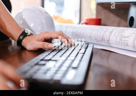 Architecture typing on keyboard for working and safty helmet, planing design on the table. Stock Photo