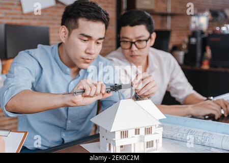 Engineering hands hold vernier caliper working and checking house model scale between meeting with businessman and businesswoman. Architecture, engine Stock Photo