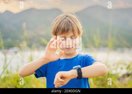 Boy uses kids smart watch outdoor against the background of the garden Stock Photo