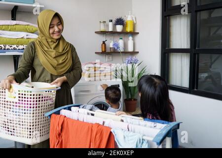 muslim asian mother and child girl little helper in laundry room near washing machine Stock Photo