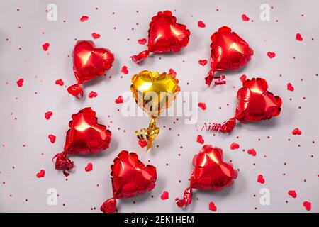 One yellow and many small red Air Balloons of heart shaped foil on festive grey background. Love concept. Holiday celebration. Valentines Day or wedding Stock Photo