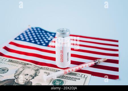 COVID-19 vaccine vials with 20 dollars bill against USA flag on blue background with copy space for text - coronavirus vaccine doses, USA vaccination Stock Photo