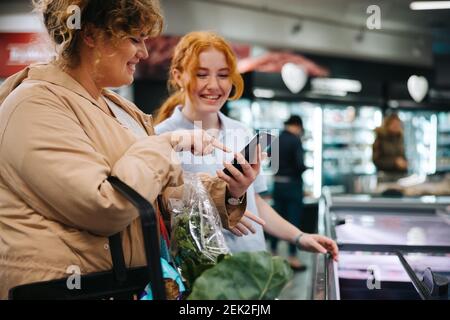 Shopper asking for help from a female worker in grocery store. Shopper asking supermarket employee for help finding a food item. Stock Photo