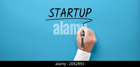 Businessman hand writing the word startup on blue background. Business start up concept. Stock Photo