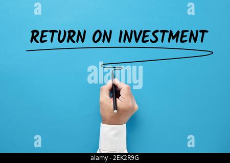Businessman hand writing return on investment on blue background. Stock Photo