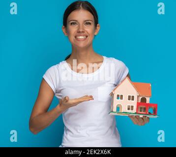 casual woman presenting a house model with a smile on her face against blue background Stock Photo