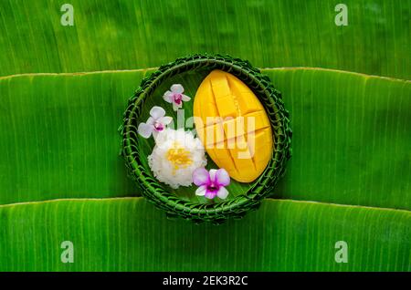 Thai dessert - mango sticky rice on banana leaf plate puts on banana leaf background. Stock Photo