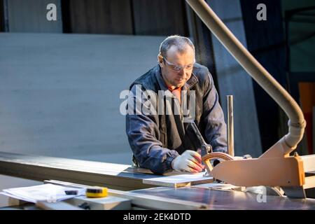 A furniture manufacturing worker at a cutting machine makes furniture parts. Furniture manufacturing. Stock Photo