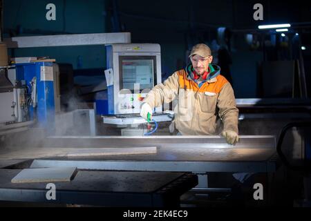 A furniture production worker behind a programmed machine makes furniture parts. Furniture manufacturing. Stock Photo