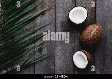 Broken coconuts on gray wooden background with palm leaf. White coconut pulp. High quality photo Stock Photo