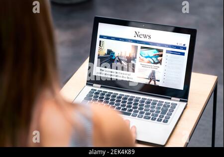 News website in laptop screen with online article and headline. Woman reading newspaper or magazine with computer. Digital web publication portal. Stock Photo