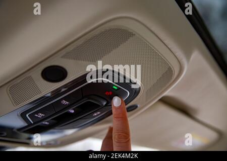female driver's finger presses sos button on the ceiling panel of a modern car Stock Photo