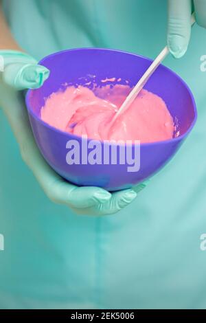 Close up of beautician's hands prepares pink alginate mask mixing in the blue bowl Stock Photo