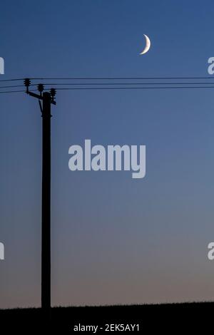 Crescent moon and telegraph pole at dusk Stock Photo