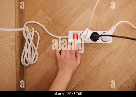 Top view of female hand turn on the extension cord at home. White cable connector Stock Photo