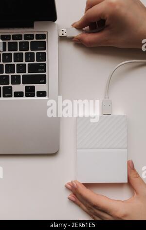 Female hand connected portable hard drive to laptop for data transfer. Backup files. Copy file. Top view Stock Photo
