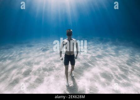 Sporty man freediver stay on sandy bottom underwater in tropical sea. Stock Photo