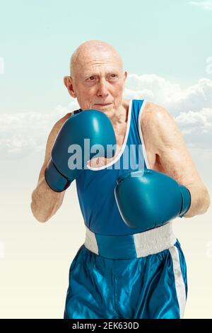 Senior man wearing sportwear boxing isolated on sky background. Caucasian male model in great shape stays active and sportive. Concept of sport, activity, movement, wellbeing. Copyspace, ad. Stock Photo