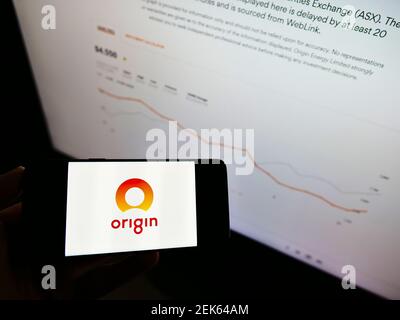 Person holding cellphone with logo of Australian energy company Origin Energy Ltd on screen in front of website with chart. Focus on phone display. Stock Photo