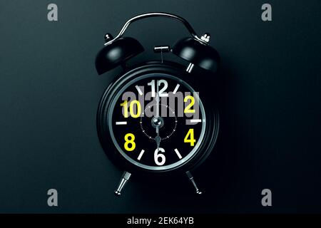 A stylish black alarm clock with yellow and white numbers stands on a dark background. Blank for the designer Stock Photo