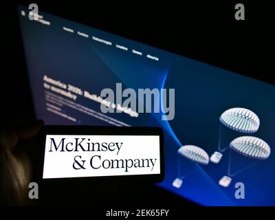 Person holding smartphone with logo of management consulting business McKinsey Company on screen in front of website. Focus on phone display. Stock Photo
